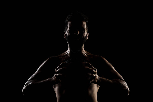 Basketball player holding a ball against black background. Side lit muscular Caucasian man silhouette. - Фото, изображение