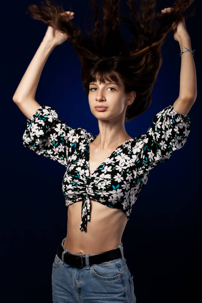 Beautiful young girl posing in studio on dark blue background. Hair in the air. - Foto, imagen