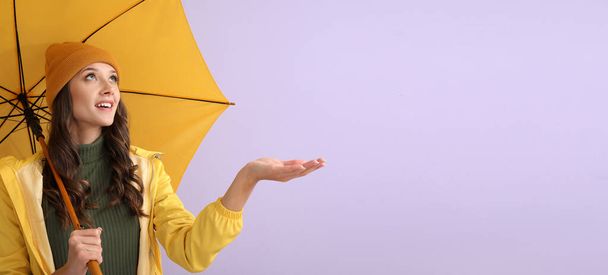 Stylish young woman in autumn clothes and with umbrella on color background with space for text - Foto, afbeelding