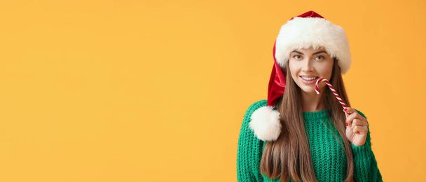 Hermosa joven en Santa sombrero y con bastón de caramelo sobre fondo amarillo con espacio para el texto - Foto, imagen