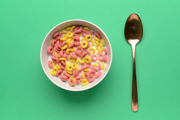 Schaal met krokante cornflakes ringen en melk op kleur achtergrond - Foto, afbeelding