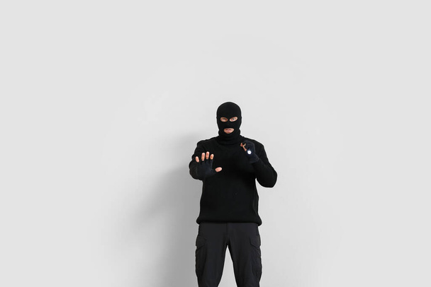 Male criminal with flashlight showing stop gesture on light background - Photo, Image