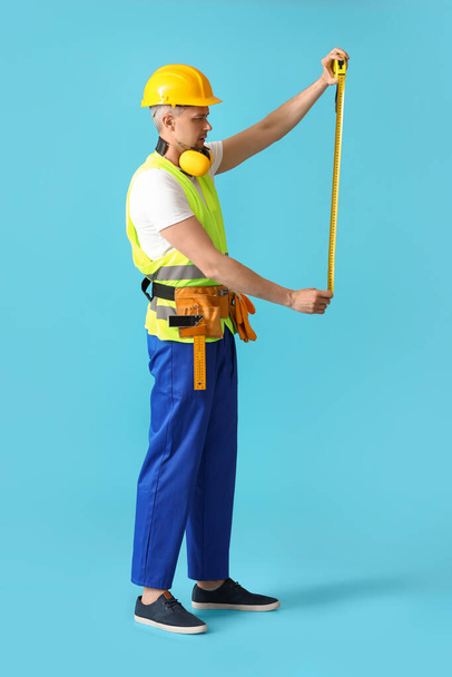 Male builder with tape measure on color background - 写真・画像
