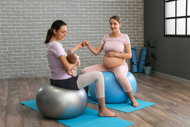 Female trainer practicing yoga with little baby and young pregnant woman at gym - Foto, Imagen