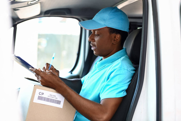 African-American courier of delivery company sitting in car - Foto, afbeelding