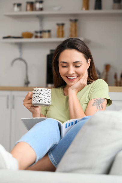 Aamulla kaunis nainen juo kahvia ja lukee lehden kotona - Valokuva, kuva
