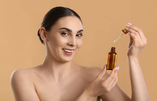 Beautiful woman opening bottle of essential oil on color background - Фото, изображение