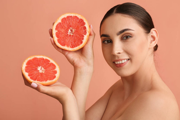 Улыбающаяся женщина держит вырезанный грейпфрут на цветном фоне - Фото, изображение