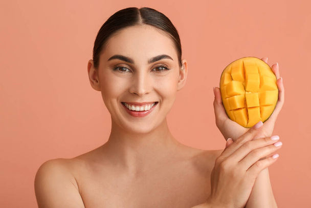 Beautiful smiling woman holding cut mango on color background - Photo, Image