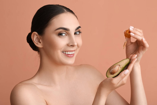 glimlachende vrouw druipt etherische olie op avocado tegen kleur achtergrond - Foto, afbeelding