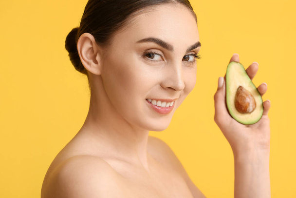 Schöne junge Frau mit gesunder Haut hält frische Avocado auf farbigem Hintergrund - Foto, Bild