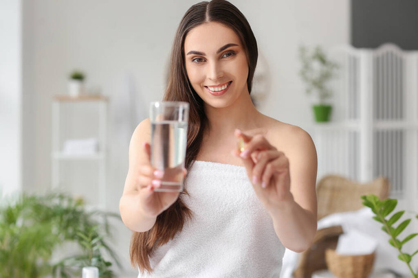 Woman holding glass of water and vitamin A capsule in bathroom - Φωτογραφία, εικόνα