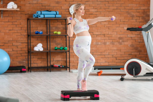 Young pregnant woman training with dumbbells and stepper in gym - Photo, image