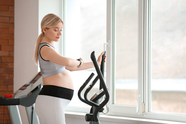 Young pregnant woman training with stair stepper in gym - 写真・画像