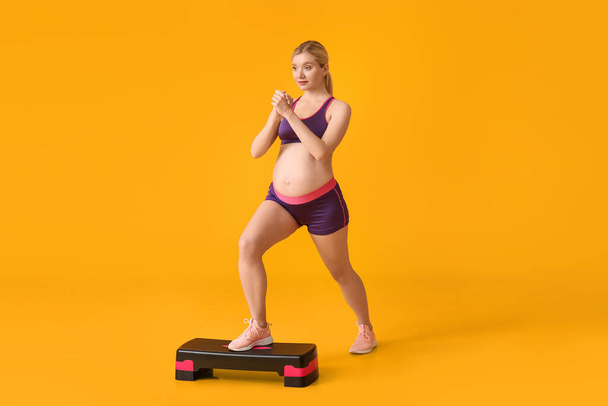 Young pregnant woman training with aerobic stepper on yellow background - Photo, image