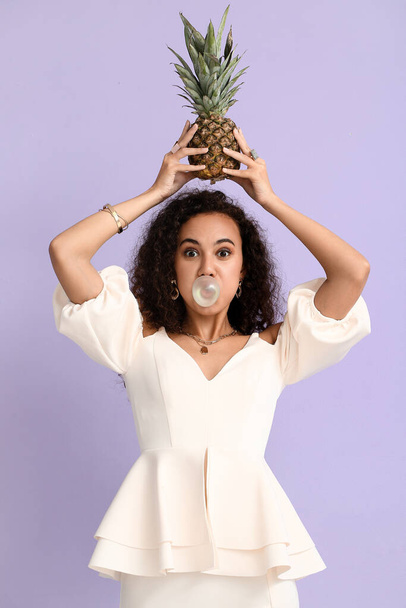Funny African-American woman with chewing gum and pineapple on color background - Fotó, kép