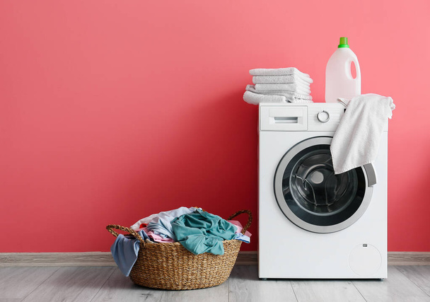 Wicker basket with laundry and washing machine near pink wall - Foto, imagen