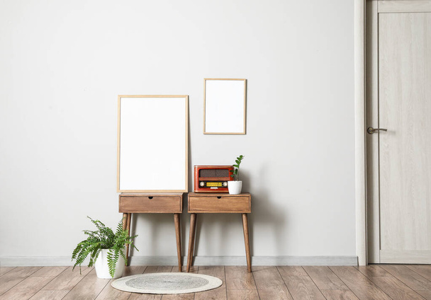 Tables with retro radio receiver, blank frames and houseplants near light wall - Photo, Image