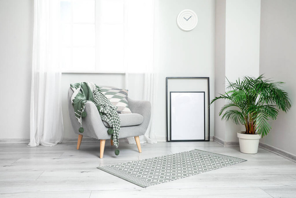 Grey armchair with plaid and blank frame near light wall - Photo, Image