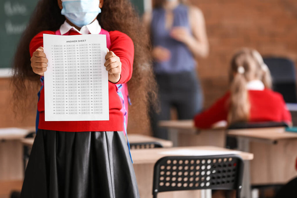 Piccola ragazza afro-americana con foglio di risposta per test scolastici in classe - Foto, immagini
