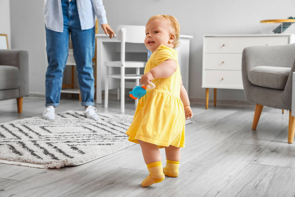 Cute baby girl in yellow dress learning to walk with mother at home - Photo, Image
