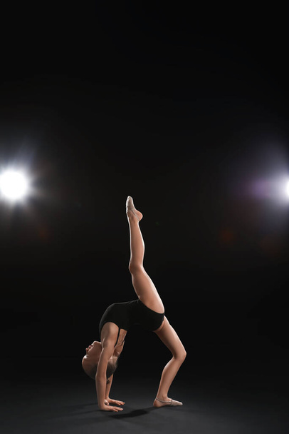 Klein meisje doet gymnastiek op donkere achtergrond - Foto, afbeelding