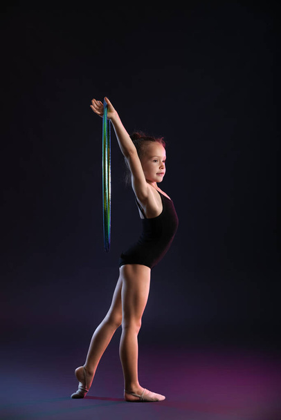 Petite fille faisant de la gymnastique avec cerceau sur fond sombre - Photo, image