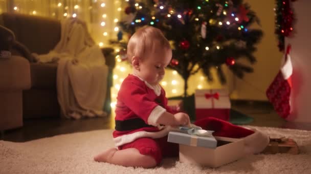 Küçük bebek Noel hediyesi kutusunu açar ve içine bakar. Aileler ve çocuklar kış tatilini kutluyor. - Video, Çekim
