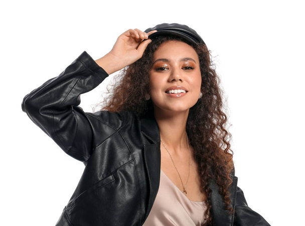 Beautiful African-American woman in stylish cap and leather jacket on white background - Photo, Image