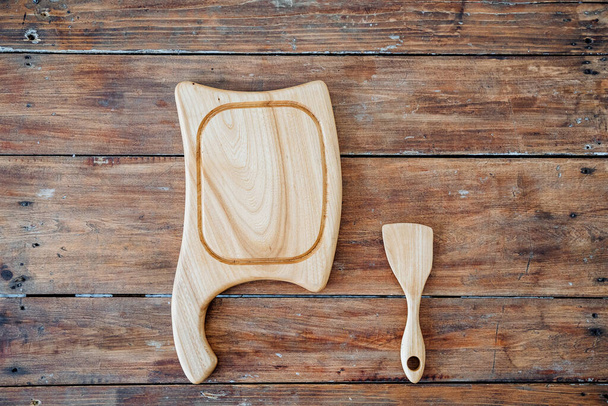Kitchen utensils made of high-quality material. A white wood cutting board and the same blade are located on a wooden table, the frame is on top. High-quality and exquisite set of utensils for the kitchen made of wood. High quality photo - Foto, imagen