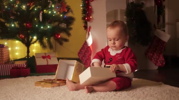 Küçük bebek Noel hediyesi kutusu ve renkli süs eşyalarıyla oynuyor. Aileler ve çocuklar kış tatilini kutluyor. - Video, Çekim