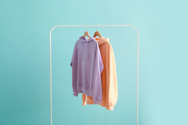 Rack with hoodies on color background - Foto, afbeelding