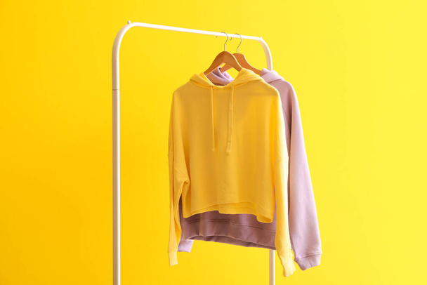 Rack with modern hoodies on color background - 写真・画像