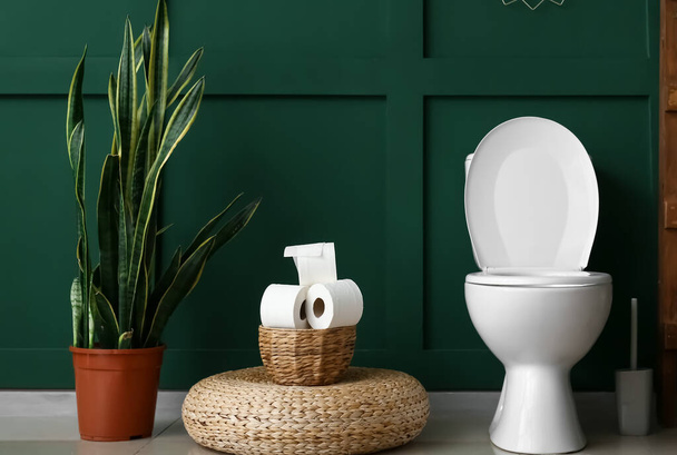 Туалетная чаша, корзина с бумагой и комод рядом с зеленой стеной - Фото, изображение