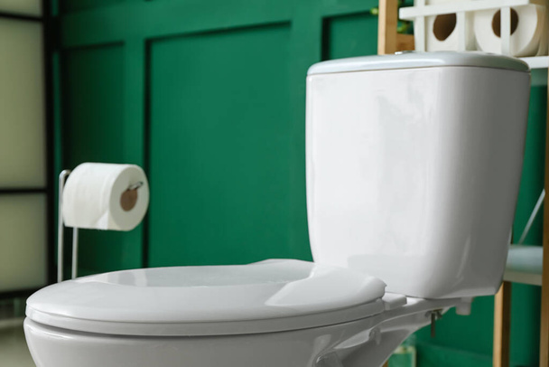 Bílá toaletní mísa v blízkosti zelené stěny na toaletě, detailní záběr - Fotografie, Obrázek