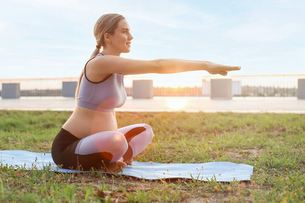 Junge schwangere Frau praktiziert Yoga im Park - Foto, Bild