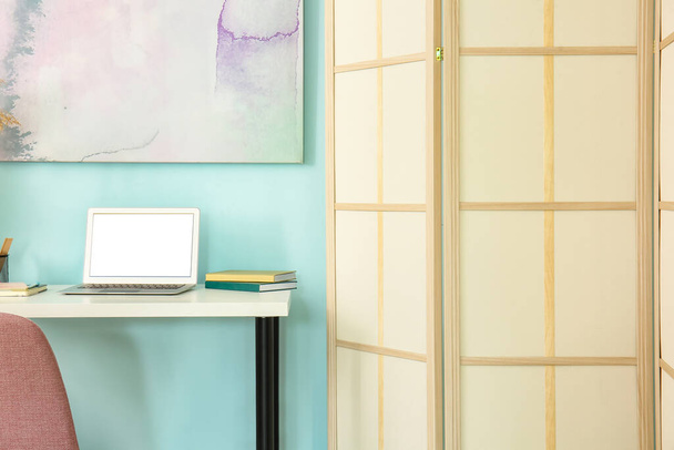 Local de trabalho moderno com laptop e tela dobrável perto da parede azul - Foto, Imagem