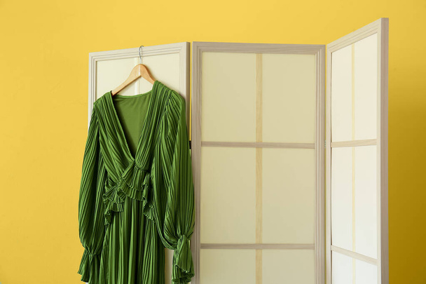 Μπεζ πτυσσόμενη οθόνη με όμορφο φόρεμα κοντά σε κίτρινο τοίχο - Φωτογραφία, εικόνα