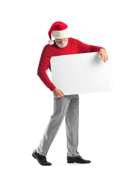 Stylish mature man in Santa Claus hat and with blank poster on white background - Photo, Image