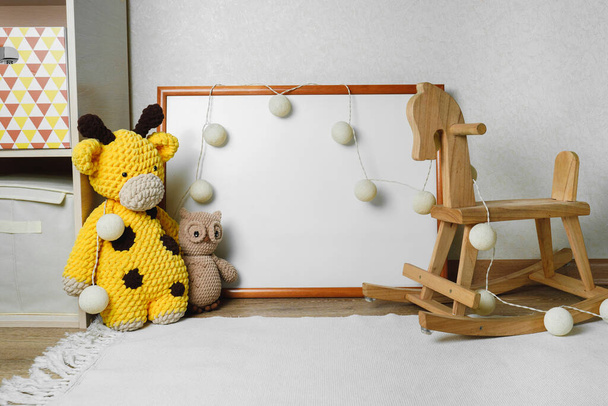 Mockup della foto nella stanza dei bambini. cavallo di legno e giocattoli a maglia. L'interno della nursery nei colori beige. - Foto, immagini