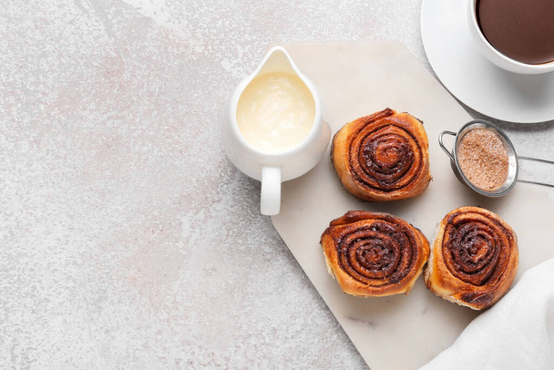 Board with tasty cinnamon rolls and cream on light background - Photo, Image