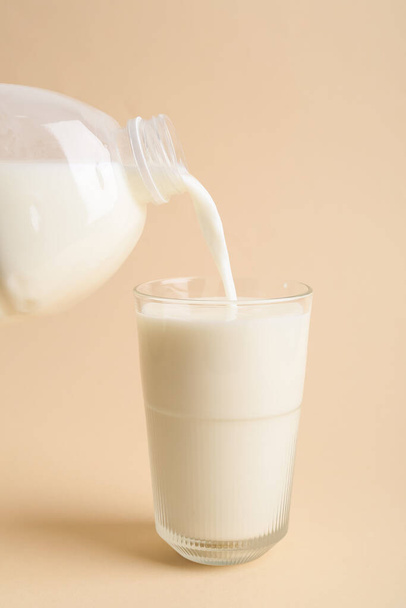Gießen von Milch aus der Gallone Flasche in Glas auf farbigem Hintergrund - Foto, Bild