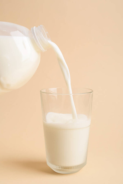 Het gieten van melk uit gallon fles in glas op kleur achtergrond - Foto, afbeelding