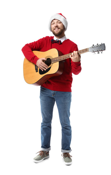 Νεαρός άνδρας στο καπέλο Σάντα παίζει κιθάρα σε λευκό φόντο - Φωτογραφία, εικόνα