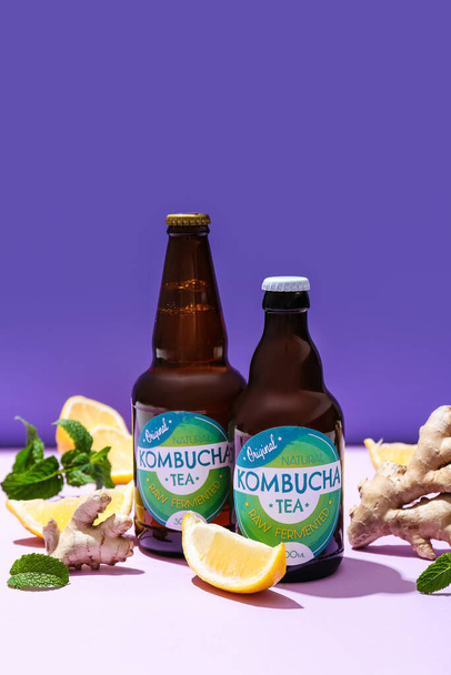Flessen van natuurlijke kombucha met citroen en gember op kleur achtergrond - Foto, afbeelding