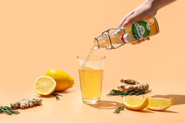 Woman pouring from bottle fresh kombucha with lemon and ginger into glass on color background - Photo, Image