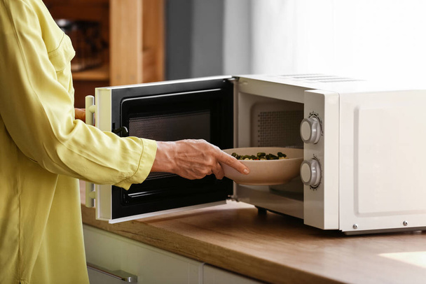 Olgun bir kadın mikrodalga fırında yemek ısıtıyor. - Fotoğraf, Görsel