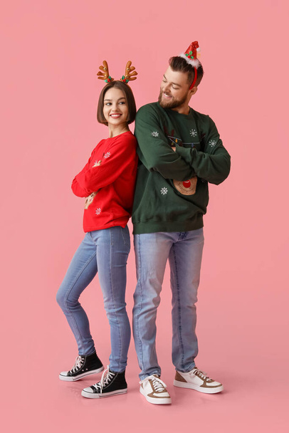 Mladý pár ve stylovém vánočním oblečení na barevném pozadí - Fotografie, Obrázek