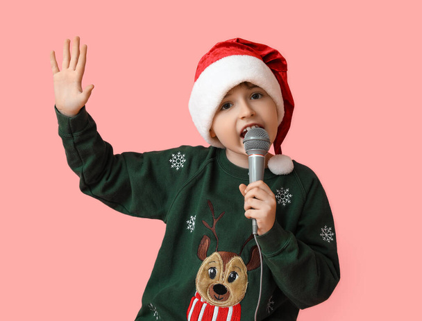 Niño en sombrero de Santa y con micrófono cantando canción de Navidad sobre fondo de color - Foto, Imagen