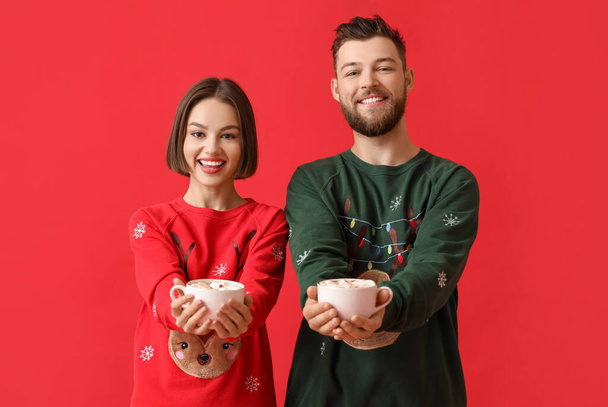 Nuori pari tyylikkäissä jouluvaatteissa ja kuppeja kuumaa kaakaota väritaustalla - Valokuva, kuva